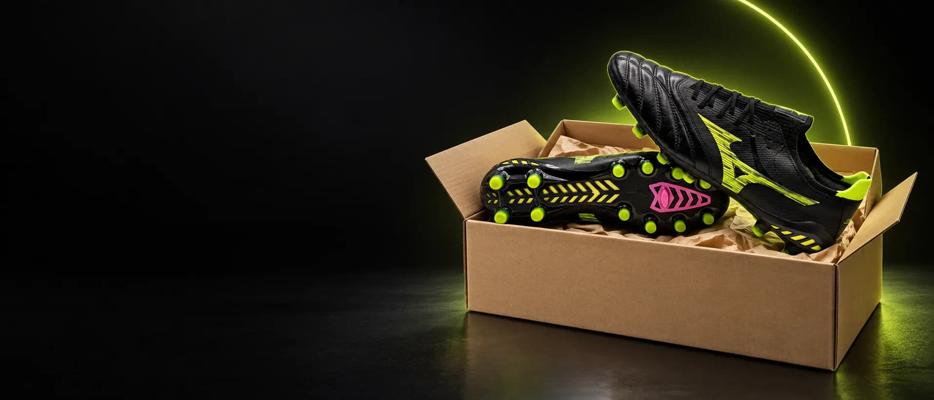 Chuteira Mizuno Morelia preta e verde-limão saindo de uma caixa de envio, com o arco verde-limão da Arena